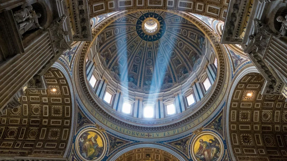 Sunlight streams through the dome of St. Peter's Basilica, revealing intricate frescoes and architecture in Vatican City.