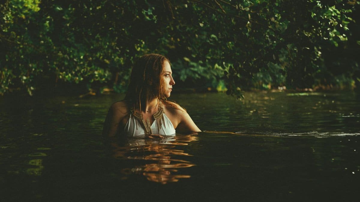 A woman peacefully immersed in a lush forest lake, bathed in warm light.
