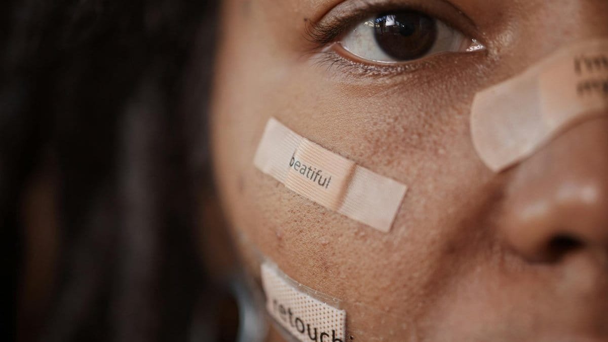 Close-up of a woman's face with band-aids featuring text, reflecting beauty and self-image themes.