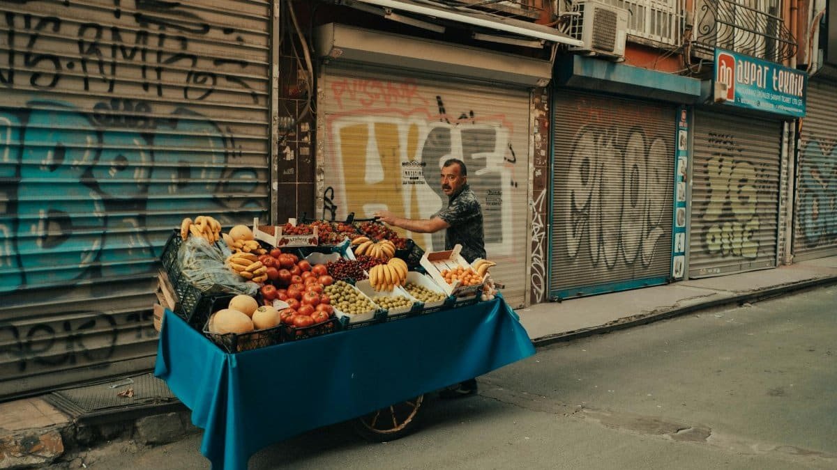 Colorful street vendor cart with fresh fruits on a graffiti-lined sidewalk.