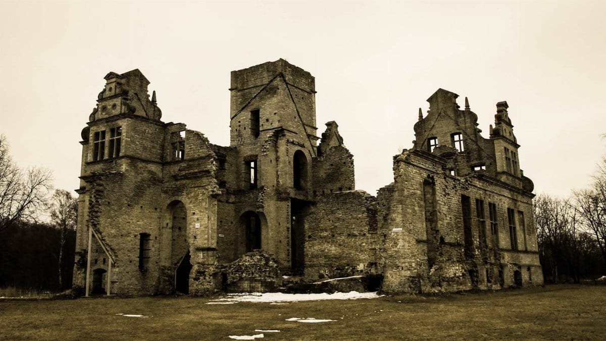A decaying stone castle ruin with leafless trees in a winter setting.