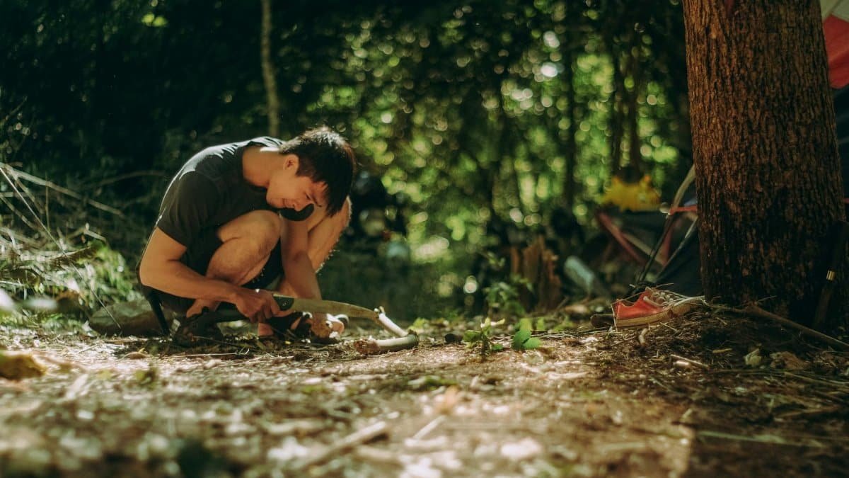 Asian man practicing bushcraft skills in a lush forest setting, surrounded by nature.