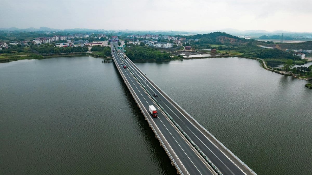 Scenic aerial shot of a bridge crossing a lake in rural China, bordered by green landscape.
