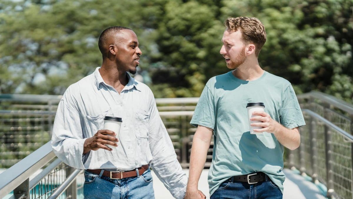 Two men holding hands and enjoying coffee on a sunny day outdoors.