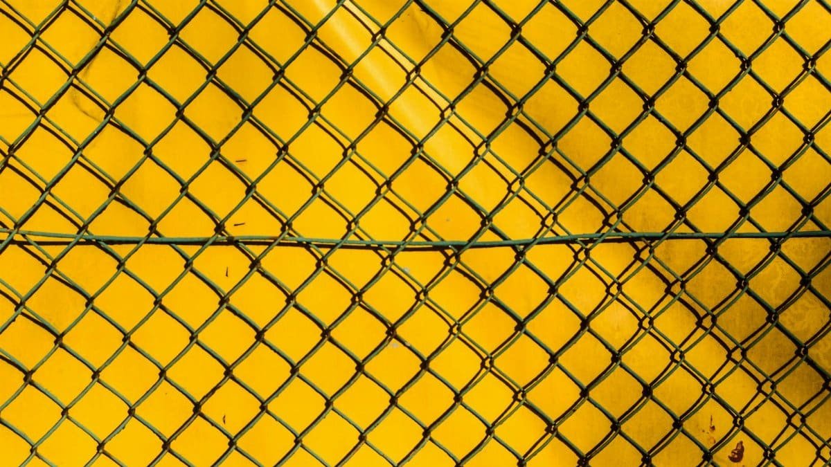 A close-up of a chain link fence against a bright yellow background, creating a stark contrast.