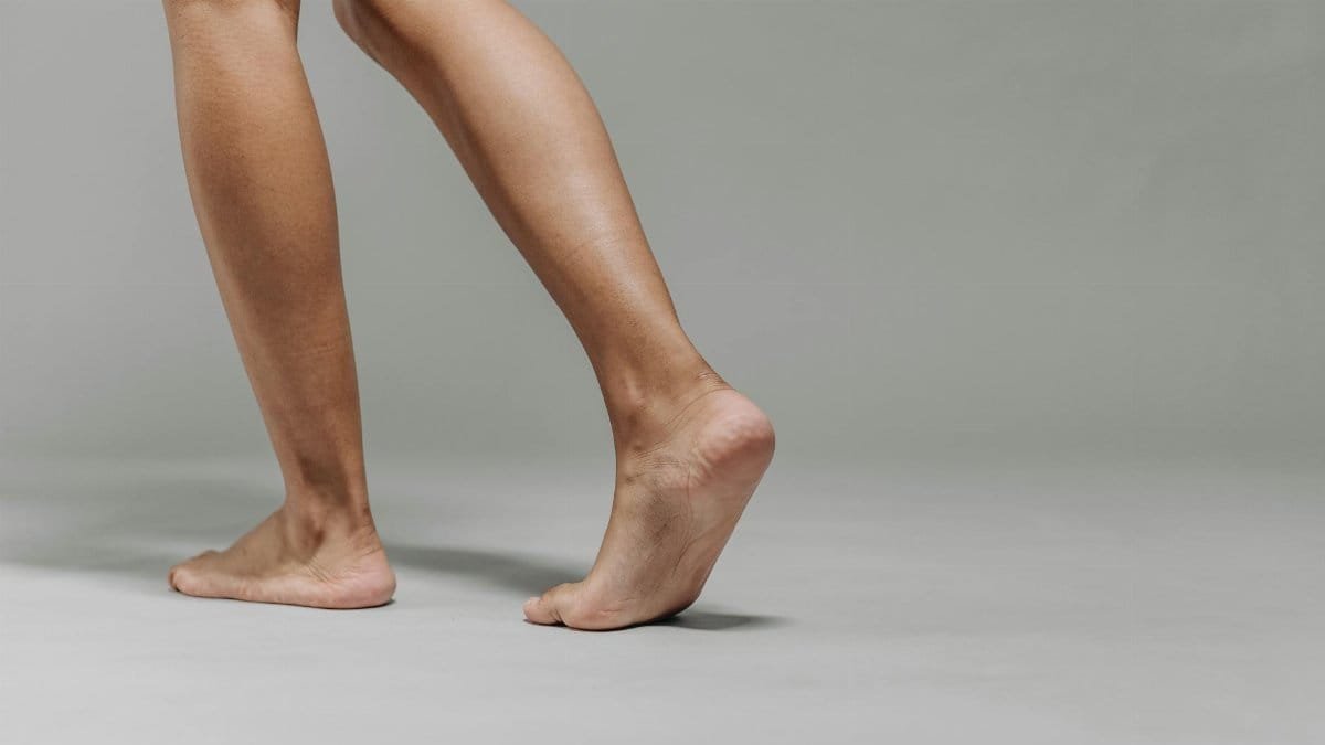 Close-up of adult bare feet on a neutral grey background, focused on walking.