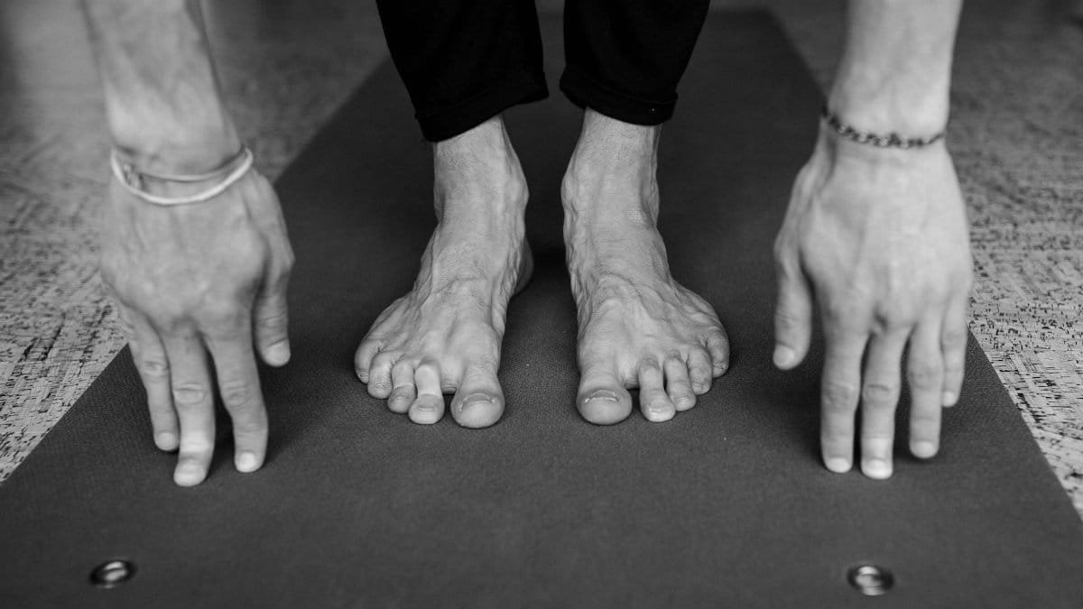 Monochrome image showing a yoga pose with focus on hands and feet stretching on a mat.
