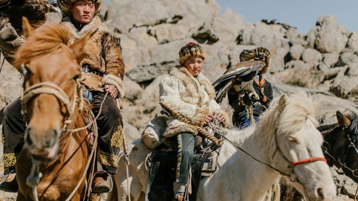 Mongolian eagle hunters in traditional attire with their birds on horseback.