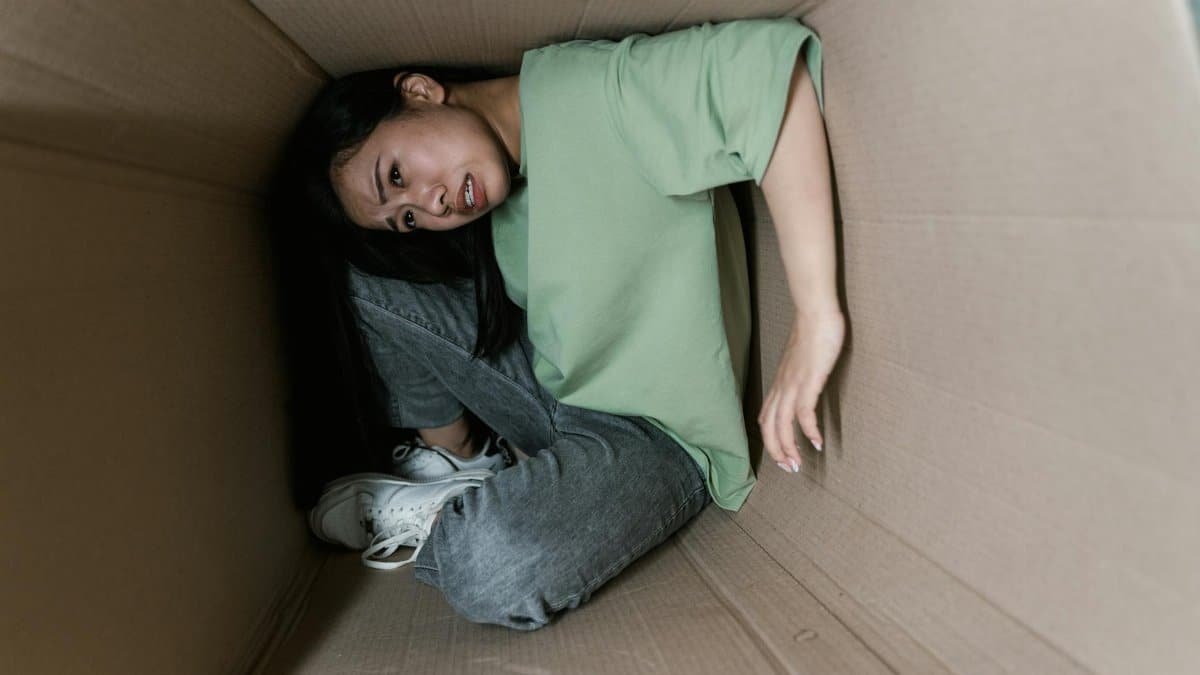 A woman trapped inside a cardboard box, symbolizing anxiety and fear.