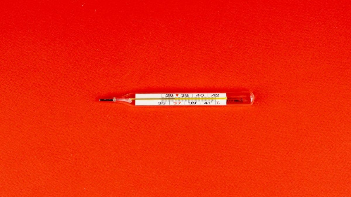 Glass mercury thermometer on a bright red surface, symbolizing health and fever measurement.