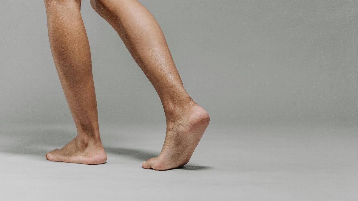 Close-up of adult bare feet on a neutral grey background, focused on walking.