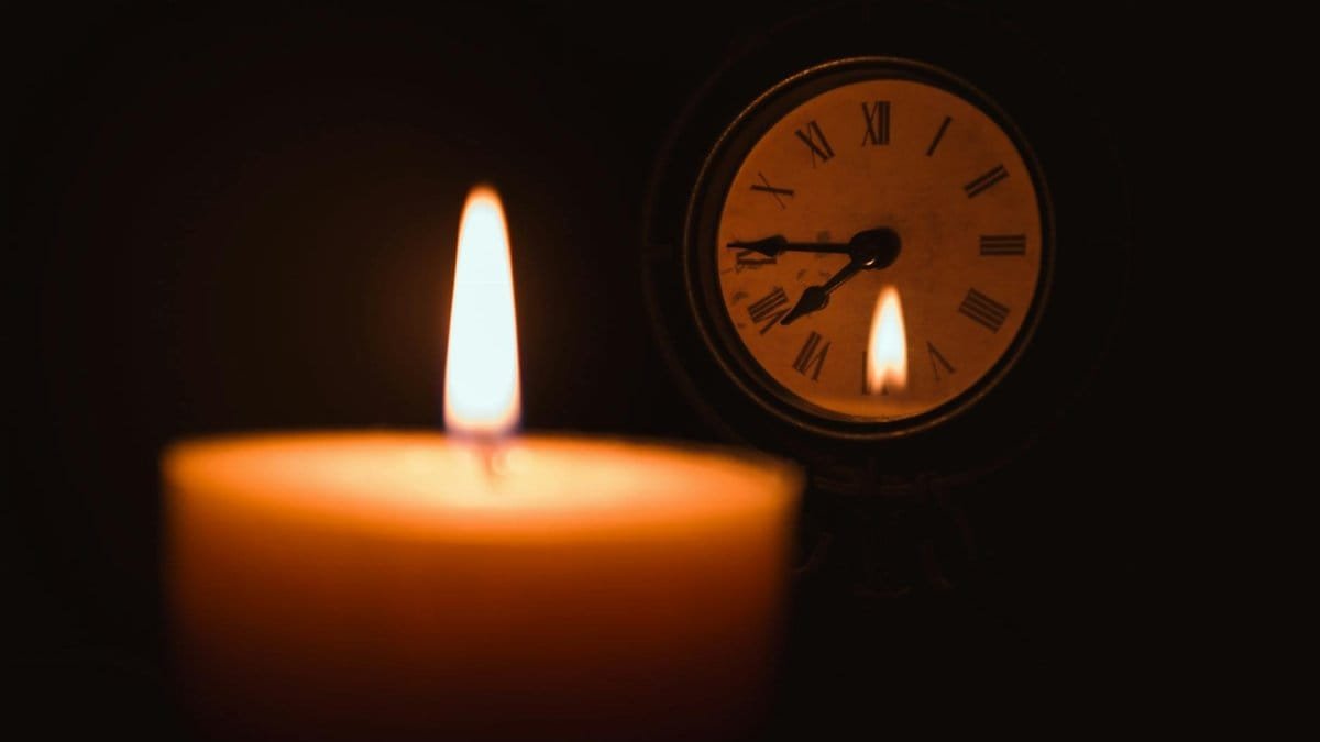 A close-up of a candle flame near a vintage clock creates a serene evening atmosphere.