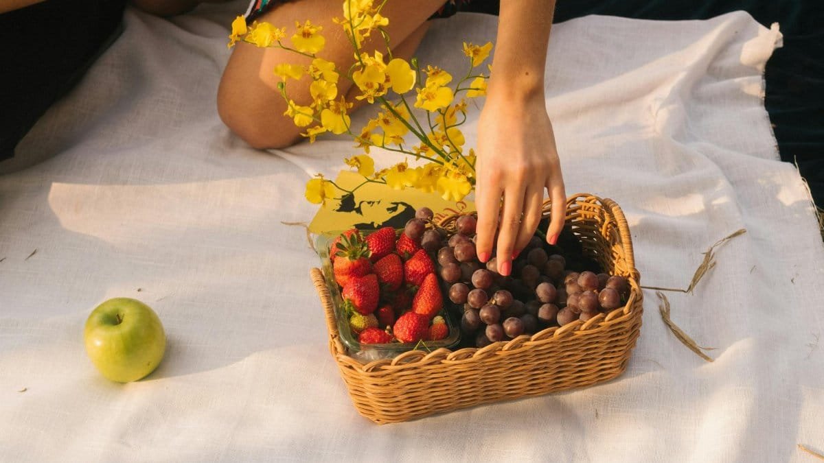 A vibrant picnic setup with strawberries, grapes, an apple, and yellow flowers in a wicker basket.