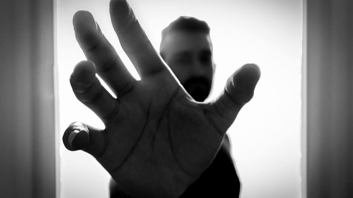 Black and white close-up of hand reaching out with blurred figure in background.