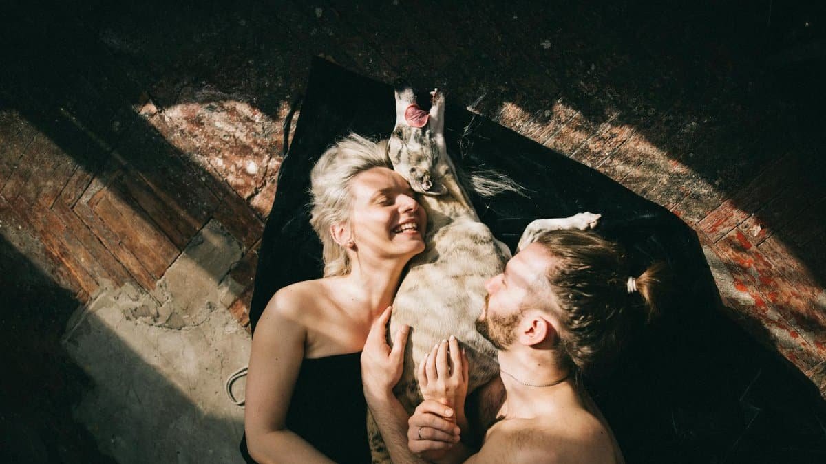 A happy couple and their dog enjoying a moment of affection and joy on the floor indoors.