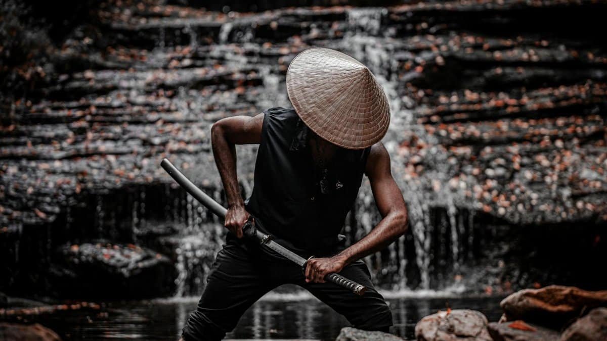 A powerful image of a samurai warrior in traditional attire, standing by a waterfall with a sword.