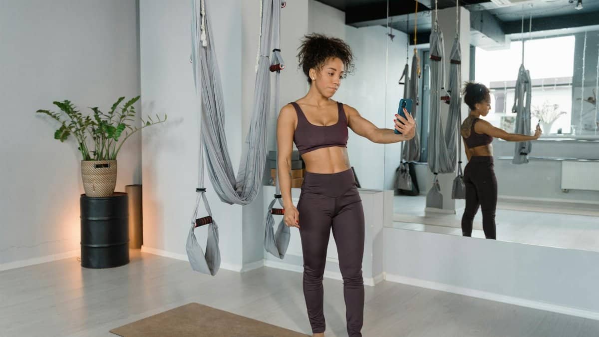 Woman in a yoga studio taking a selfie with aerial yoga hammocks, reflecting a healthy lifestyle.