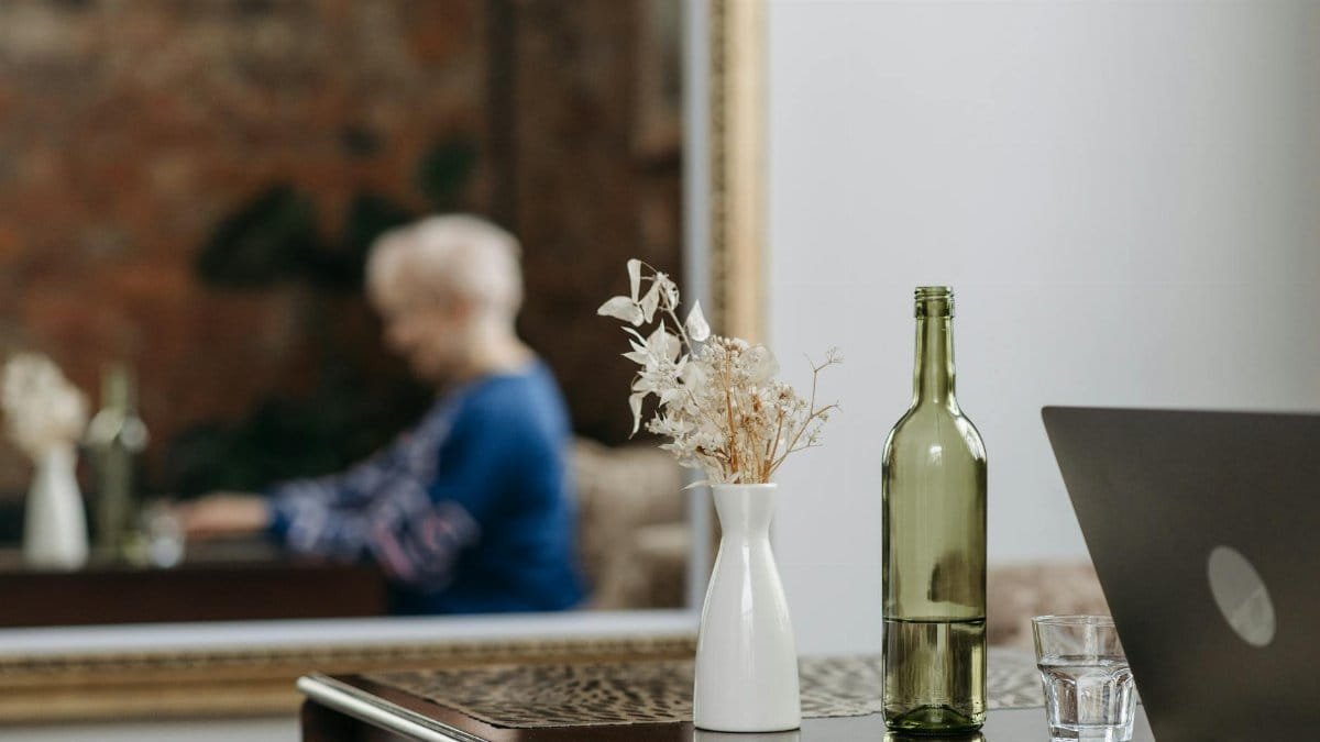 A serene indoor scene with wine bottle, glass, and reflection in the mirror.