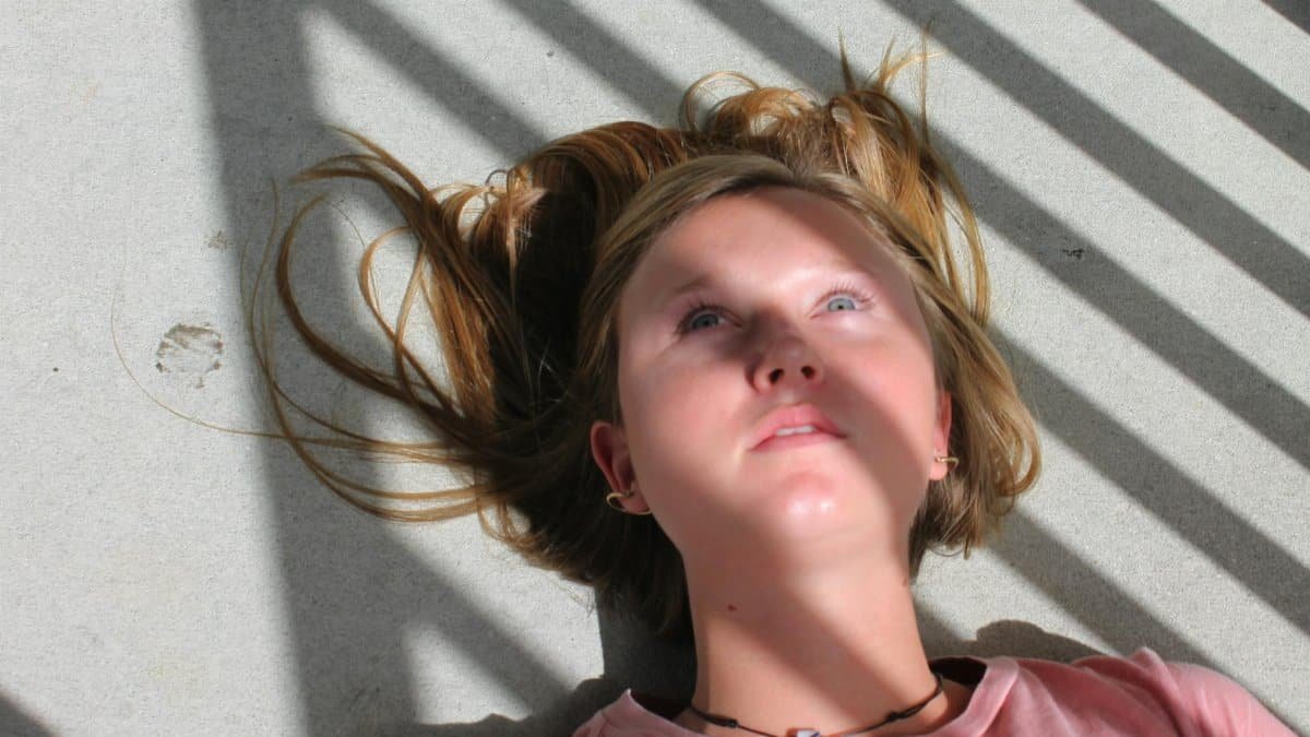 Close-up of a young woman lying on a floor with dramatic shadows and sunlight casting across her face.