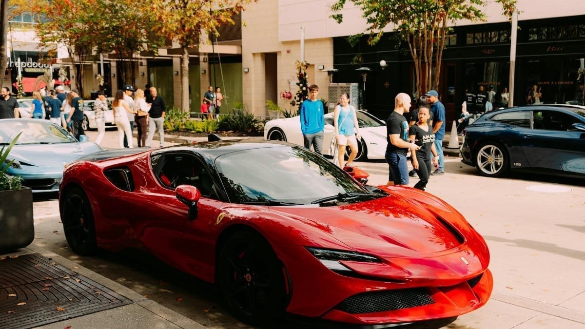 Luxurious red Ferrari parked street side with people walking by.