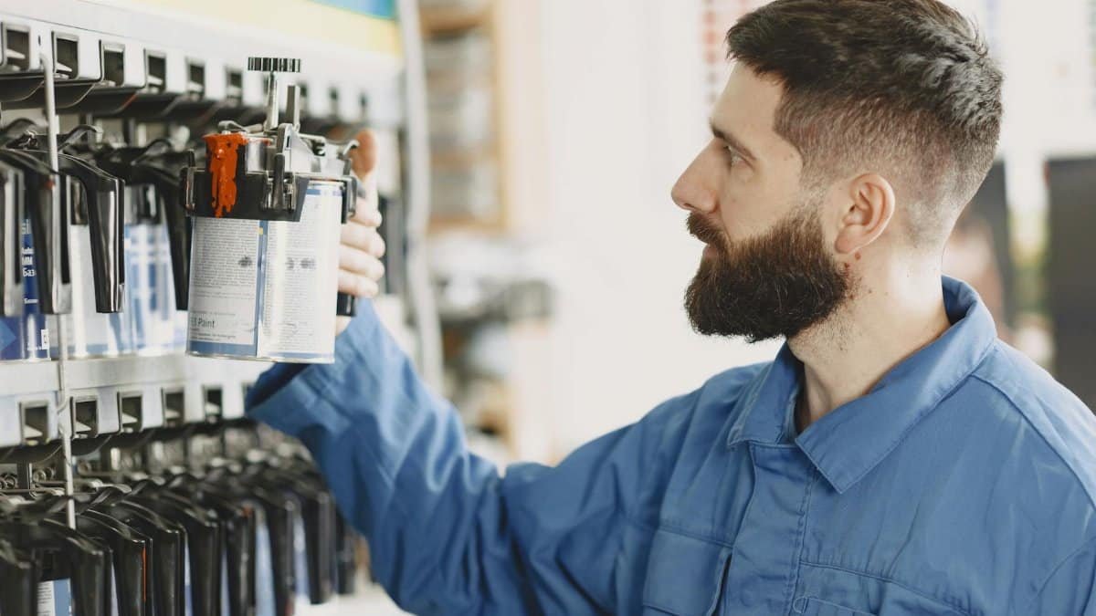 Mechanic in blue overalls choosing a paint can from a shelf in the workshop.