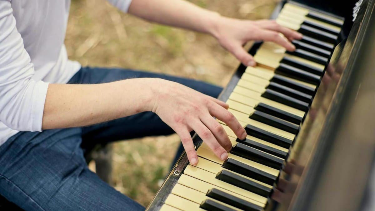 A close-up of a person playing piano outdoors, focusing on hands and keys.