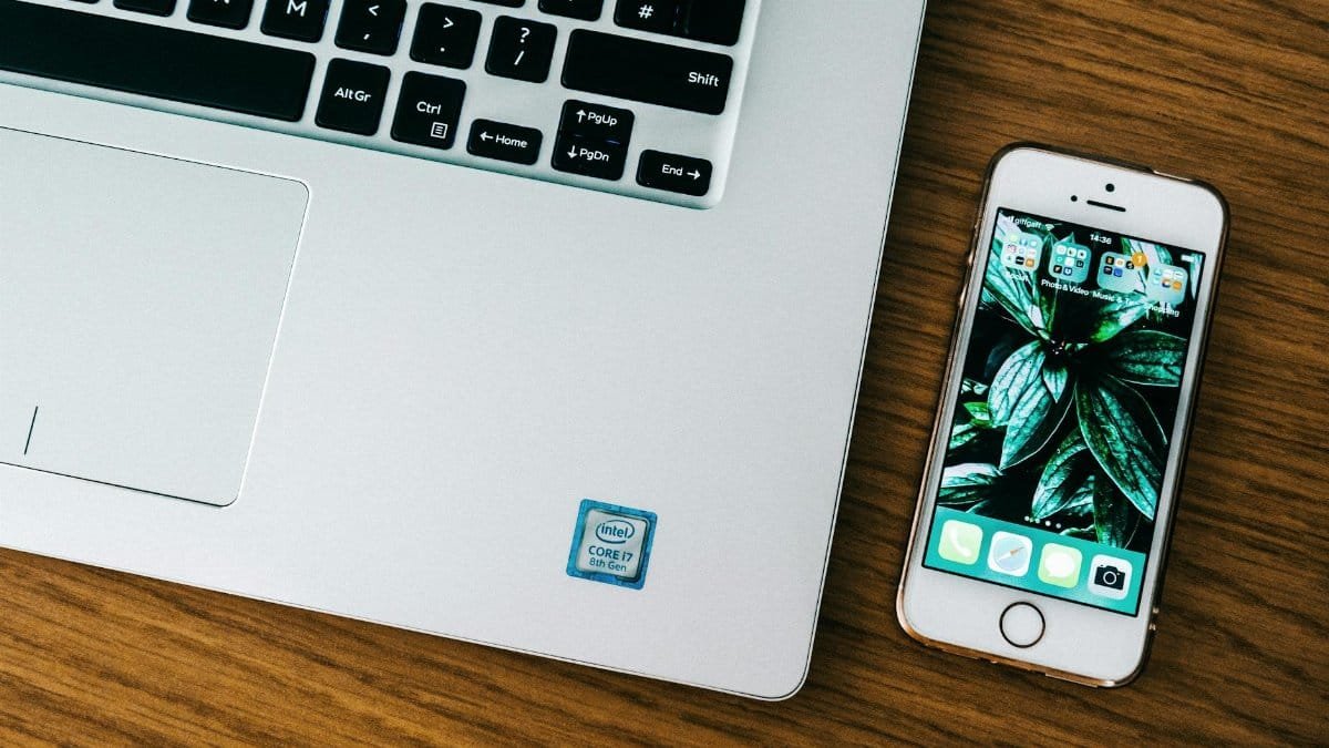 Close-up of a laptop and smartphone on a wooden desk in an office setting.