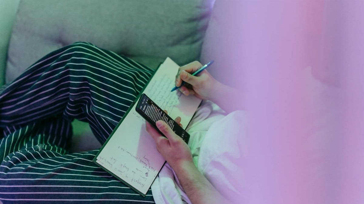 A cozy scene of a person writing notes in a notebook while using a smartphone.