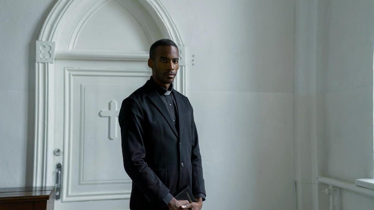 Young male minister stands confidently holding a book in front of a church door.