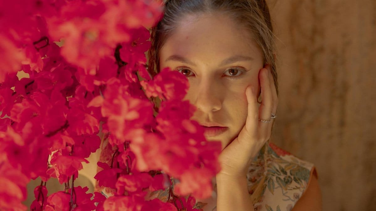 Candid portrait of a woman surrounded by vibrant red flowers indoors.