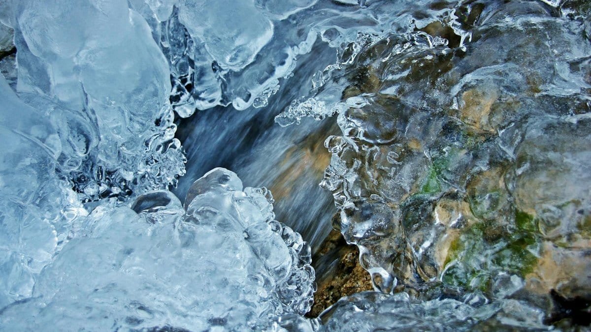 Detailed macro shot of ice formation over a flowing stream, capturing winter's natural beauty.