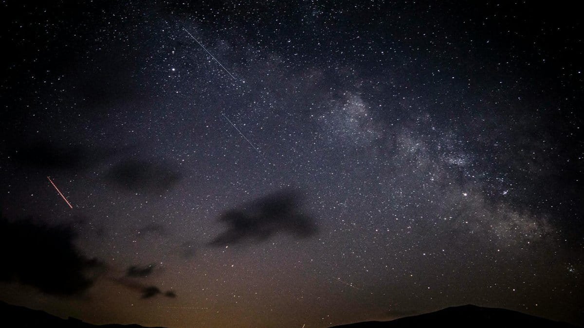 A stunning night sky showcasing stars, clouds, and the Milky Way galaxy with a visible meteor shower.