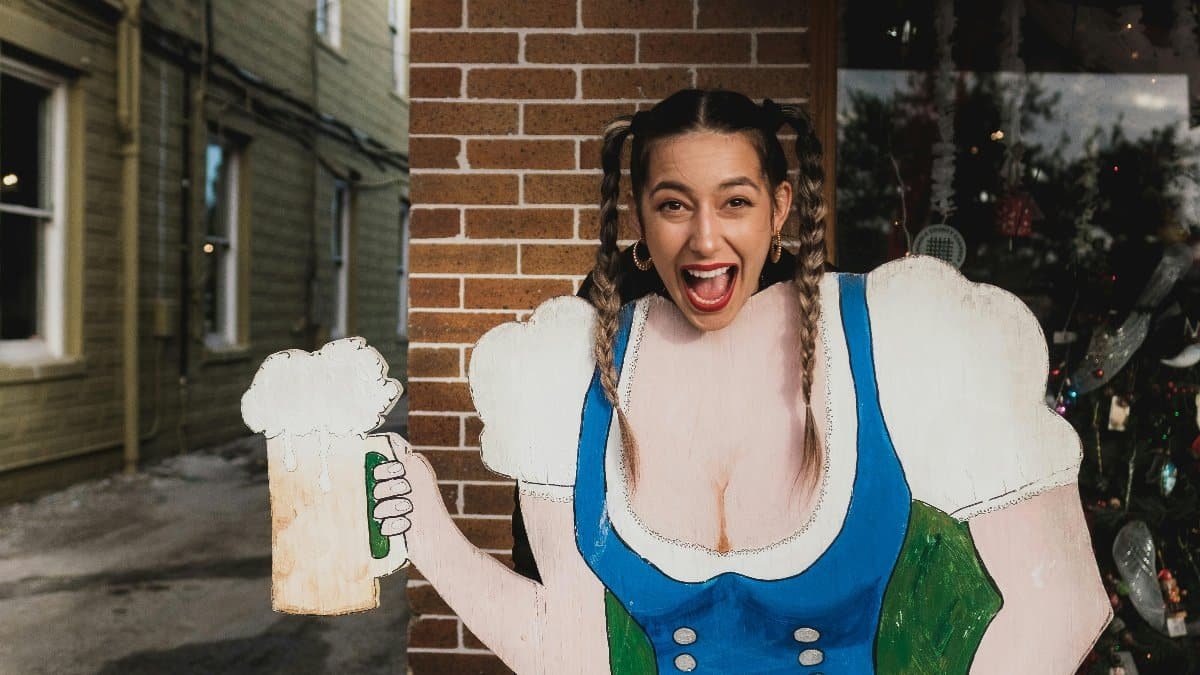 Festive woman smiling with Oktoberfest cutout in Sanford's city streets. via Pexels