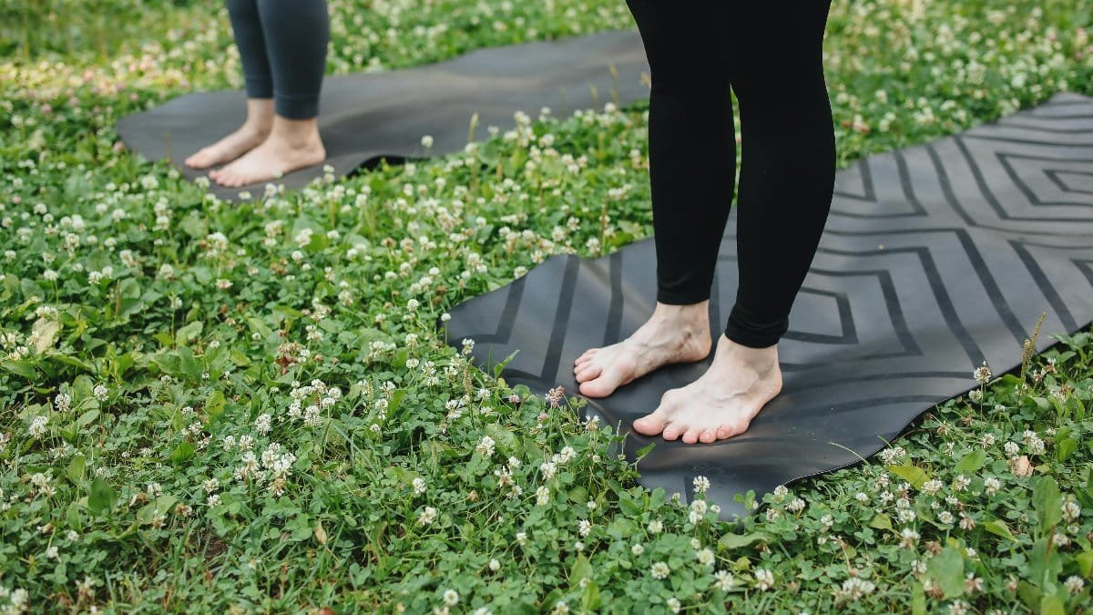 Two people practicing yoga barefoot on mats in a grassy park.