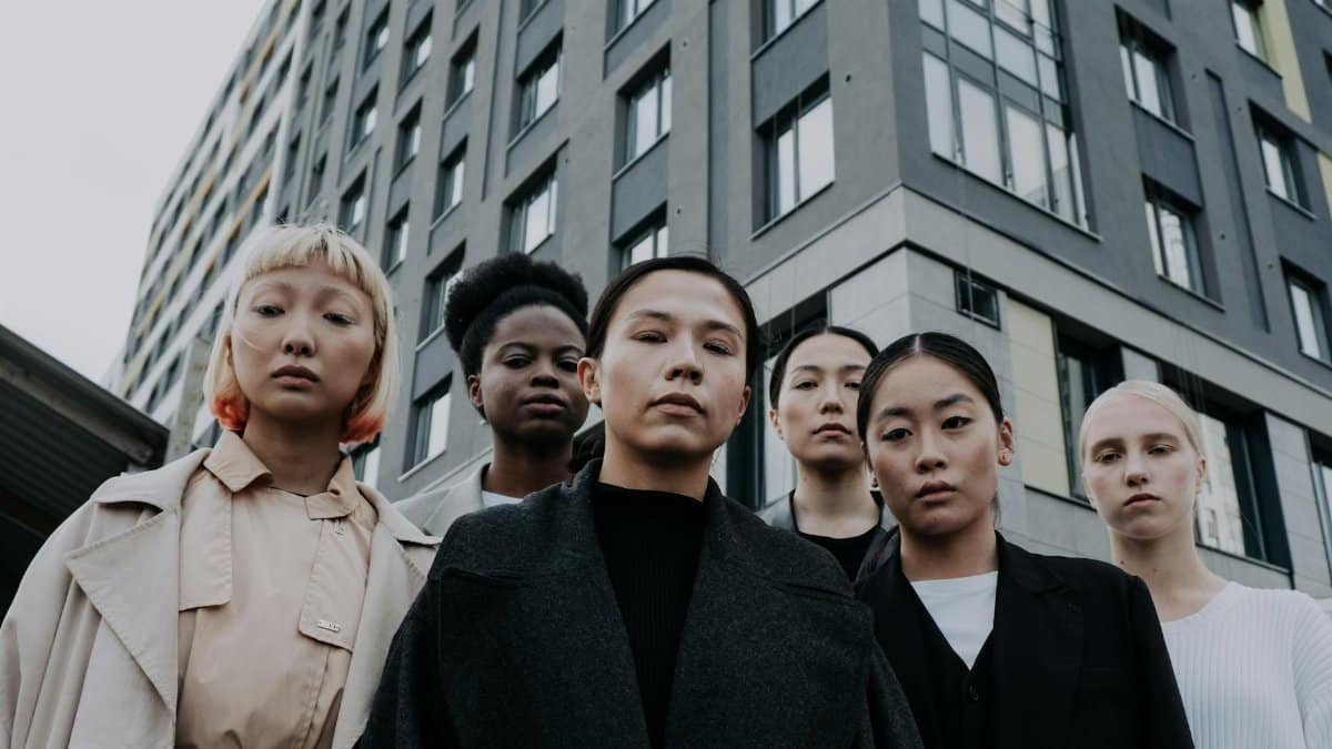 Strong and diverse group of women stand confidently in front of a modern apartment building.