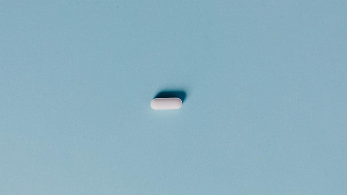 Single white pill on a blue background, representing medicine or healthcare.