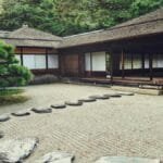 Serene Japanese Zen garden with stone path, lush greenery, and traditional wooden architecture.