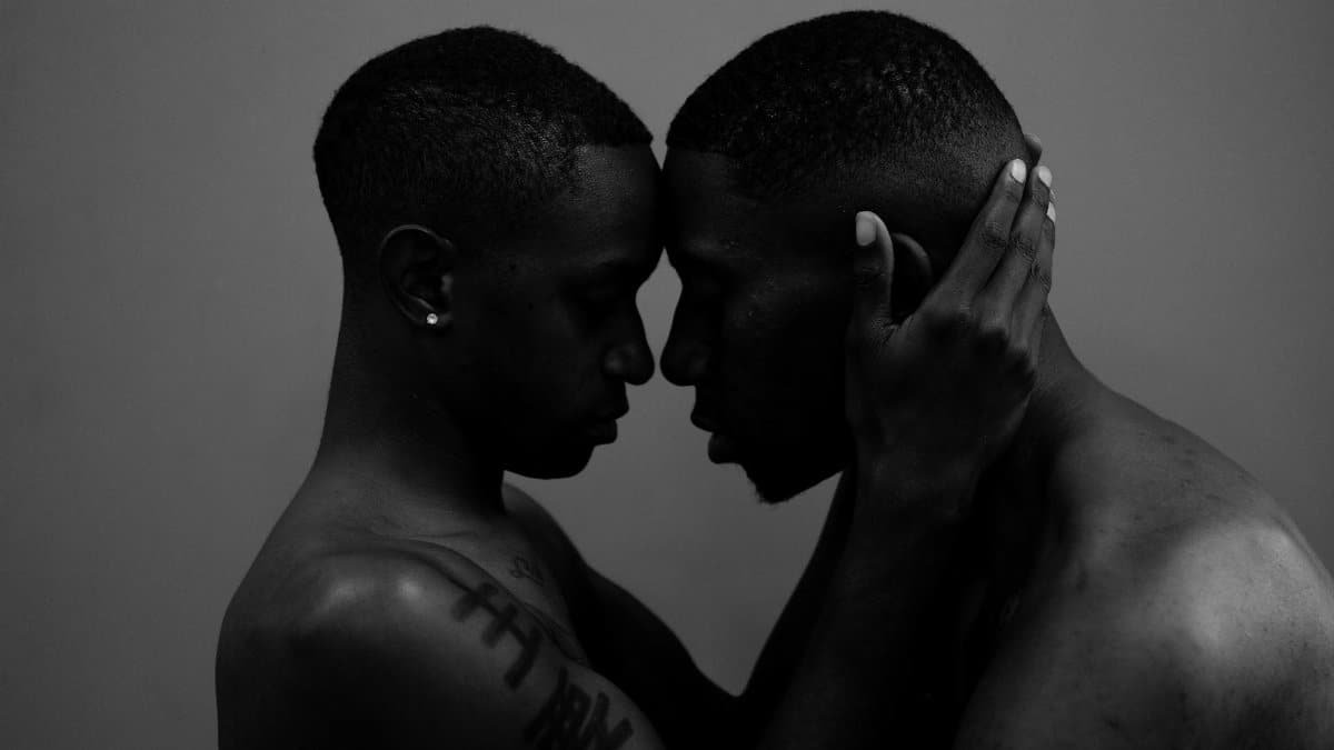 Black and white close-up of two men sharing an intimate embrace in a monochromatic setting.