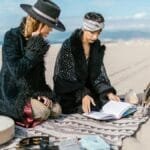 Two women performing a spiritual ritual on a sandy beach with crystal and book.