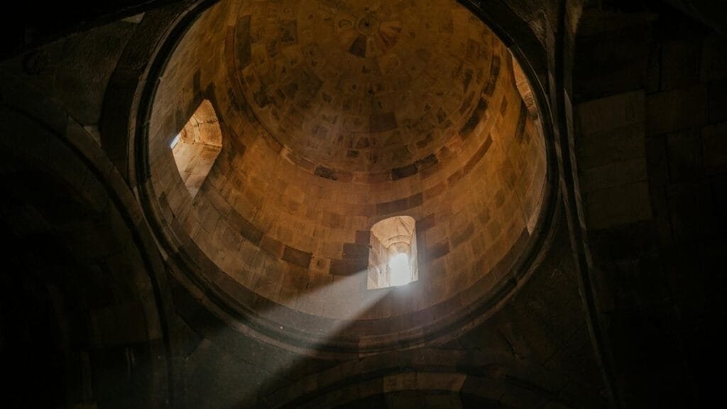 From below of bright sunshine illuminating through window of dome in ancient stone cathedral