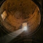 From below of bright sunshine illuminating through window of dome in ancient stone cathedral