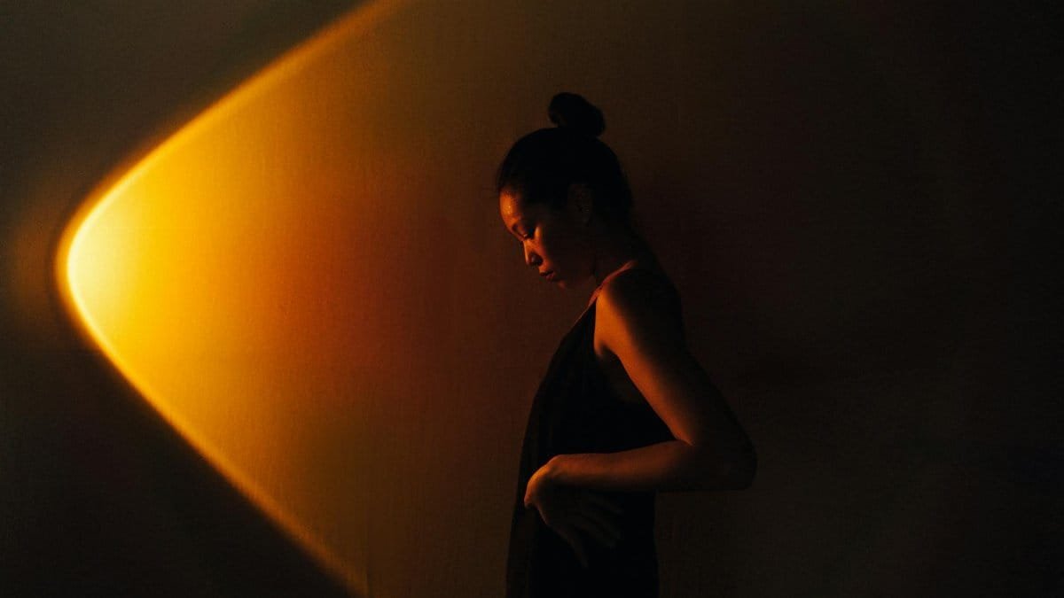 Side profile of an Asian woman in a dark studio setting with dramatic lighting.
