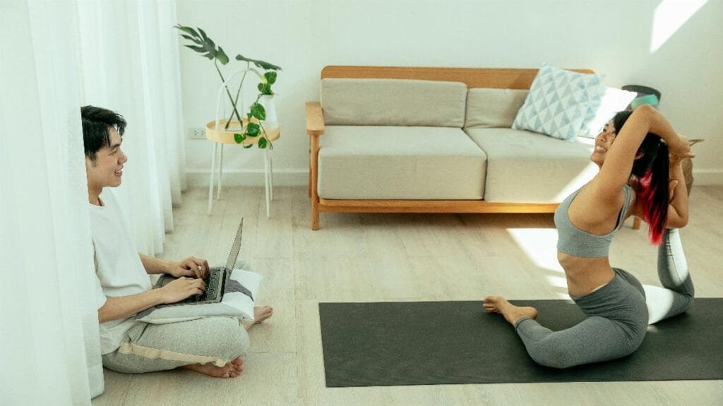 A couple practicing yoga and working on a laptop in a modern living room, embracing wellness.