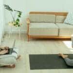 A couple practicing yoga and working on a laptop in a modern living room, embracing wellness.