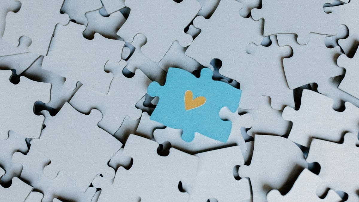 A standout blue puzzle piece with a heart symbol among white puzzle pieces, showing uniqueness.