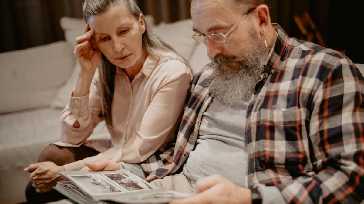A senior couple reminisces while looking through a photo album at home, reflecting on cherished memories.