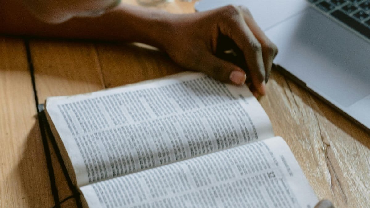 A young adult reading the Bible beside a laptop, deep in study. via Pexels