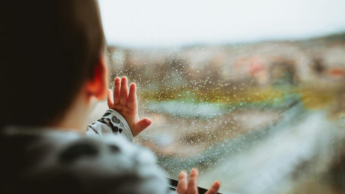 A young child gazes outside through a rainy window, capturing a moment of curiosity and wonder.