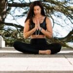 Woman practicing meditation in nature amidst stone columns, promoting peace and mindfulness.
