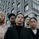 Strong and diverse group of women stand confidently in front of a modern apartment building.